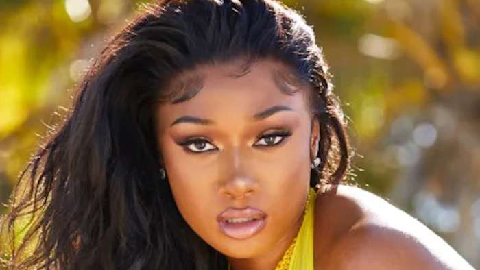 Megan Thee Stallion poses in front of a vibrant green backdrop in a bright yellow swimsuit.